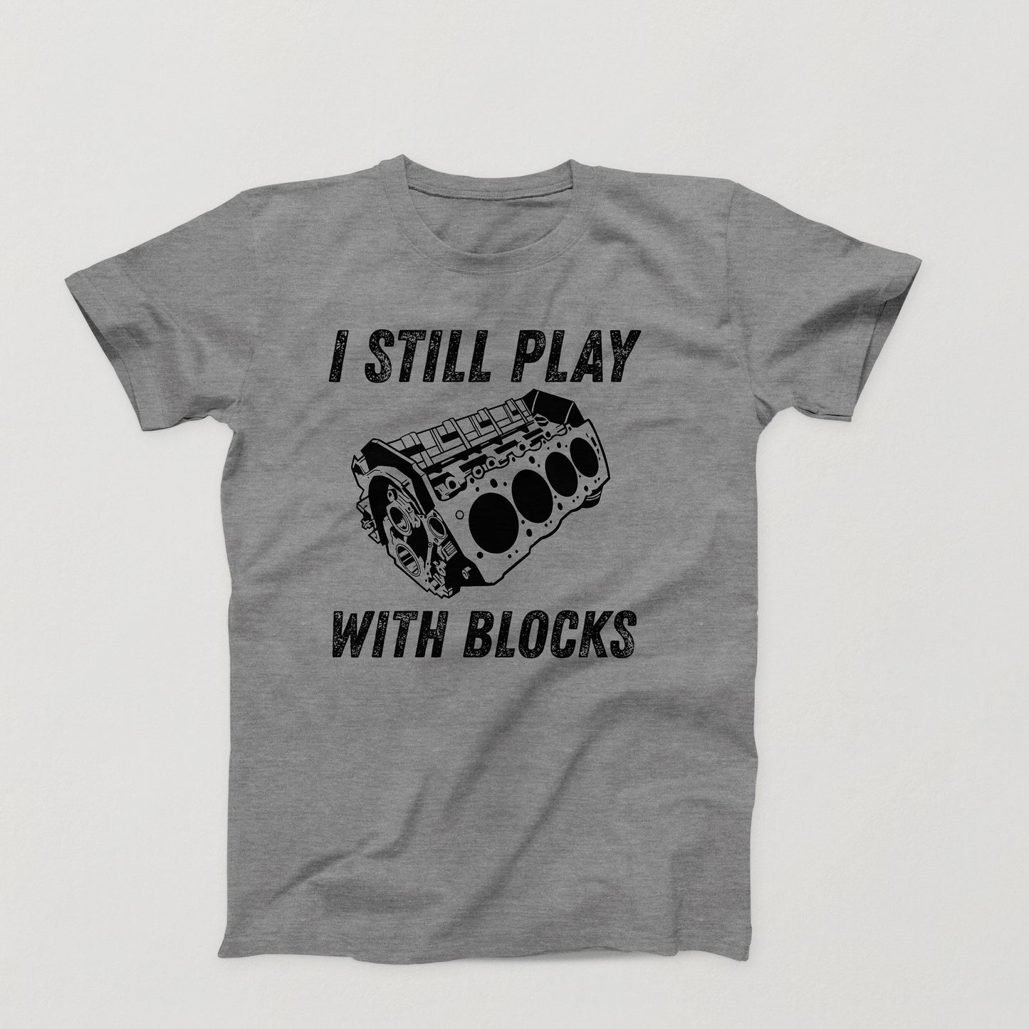 gray t-shirt design with white V8 engine block and the phrase “I Still Play With Blocks” in distressed text