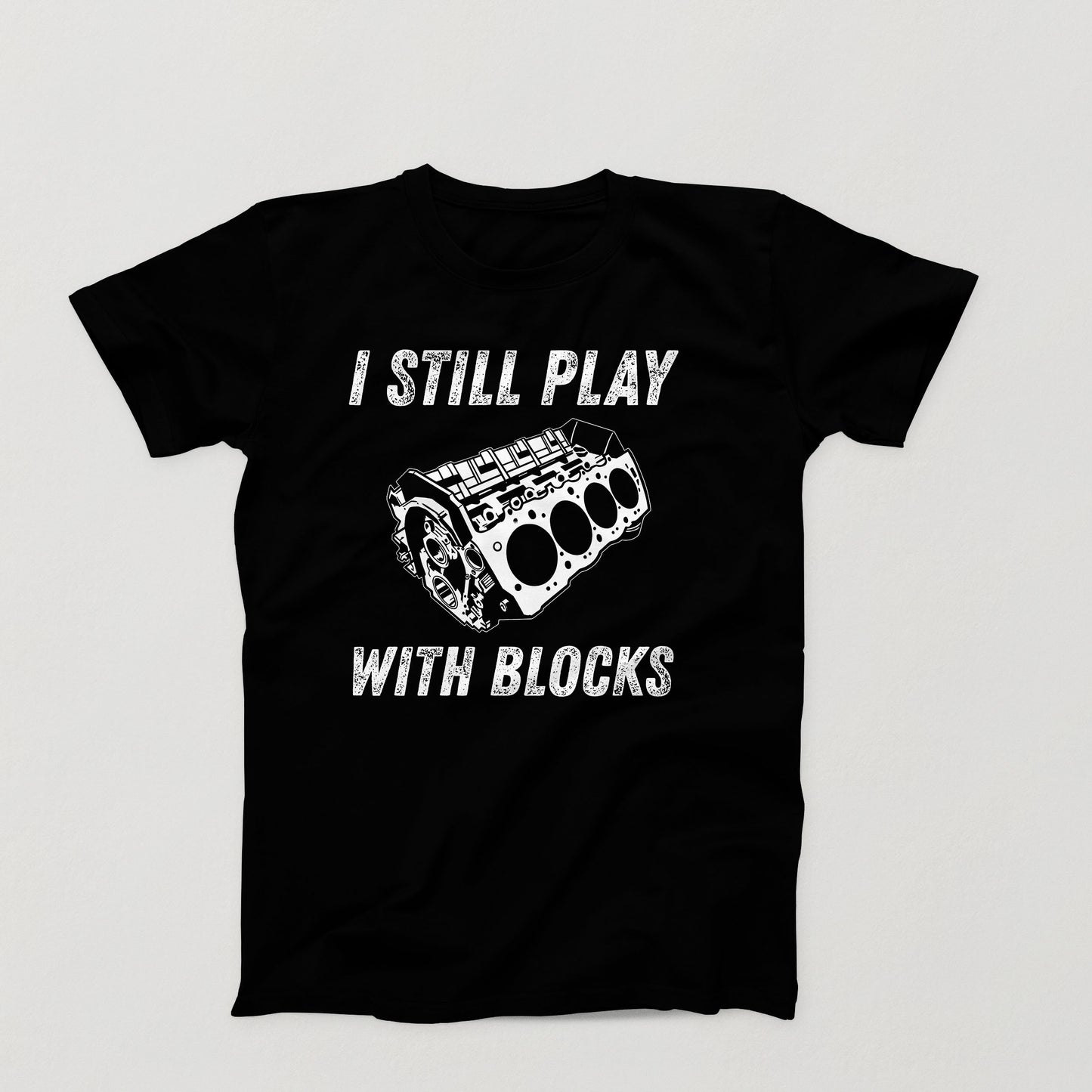 Black t-shirt design with white V8 engine block and the phrase “I Still Play With Blocks” in distressed text