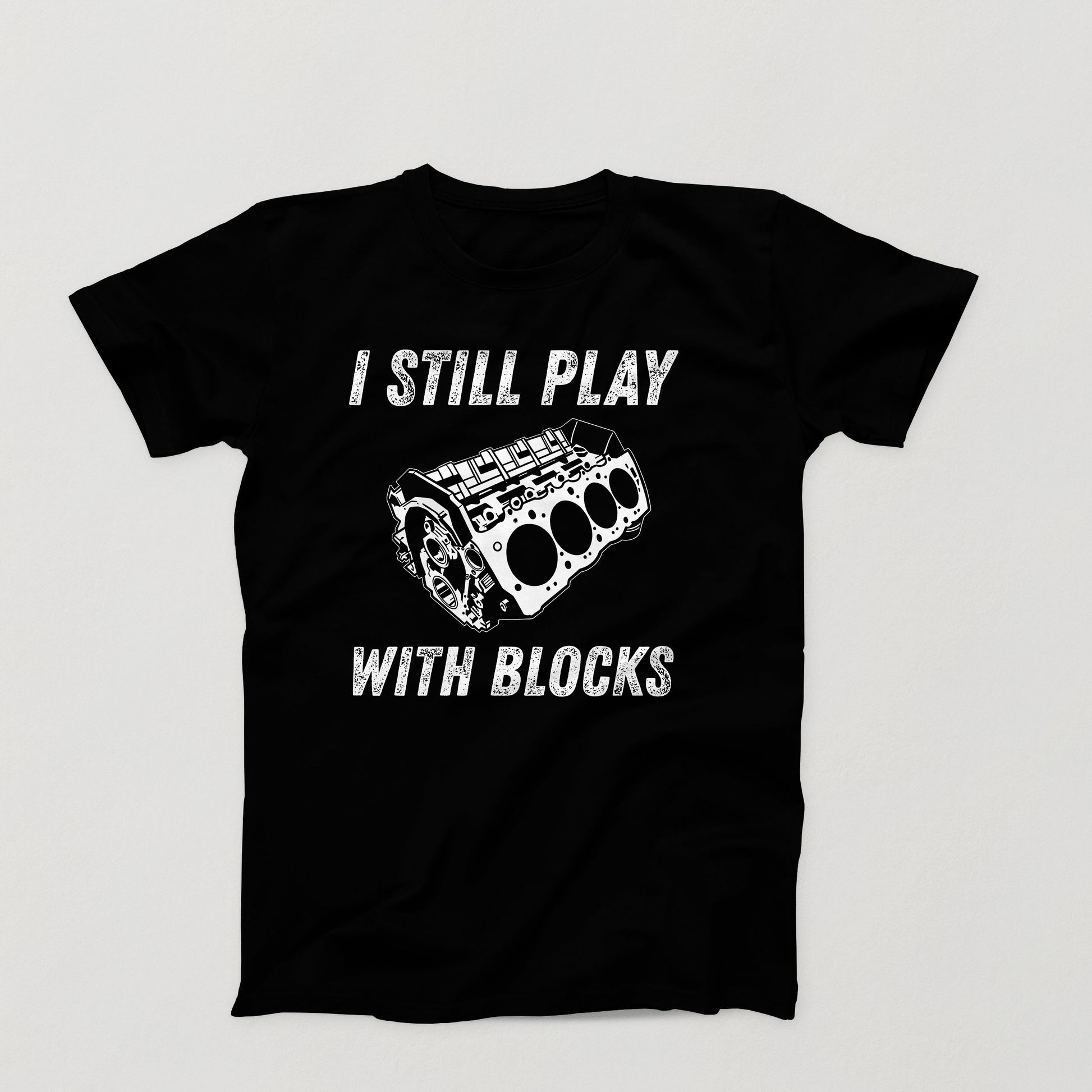 Black t-shirt design with white V8 engine block and the phrase “I Still Play With Blocks” in distressed text