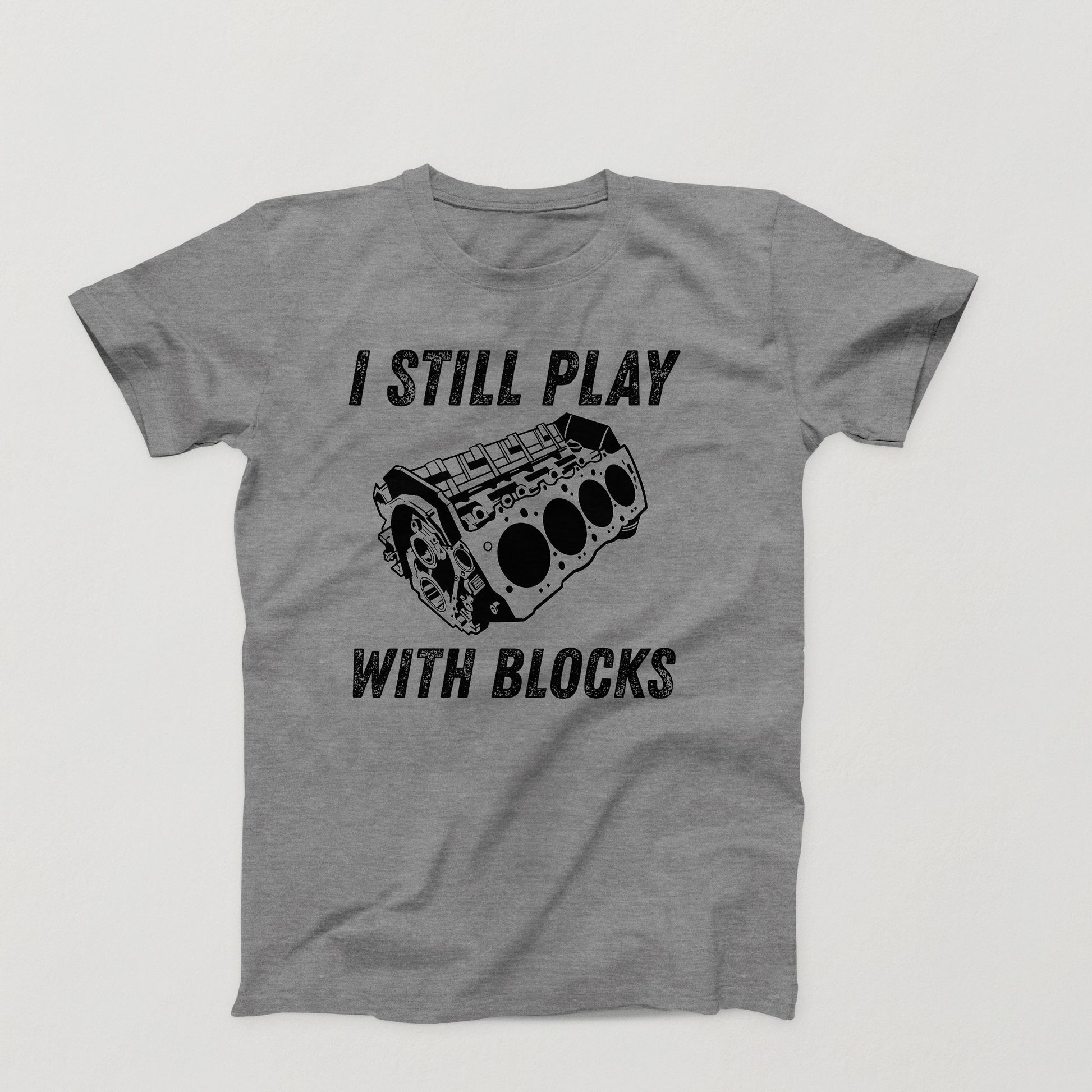 gray t-shirt design with white V8 engine block and the phrase “I Still Play With Blocks” in distressed text